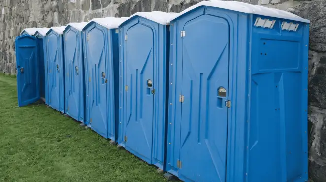 Row of blue portable toilets lined up on grass against a stone wall for event sanitation in Chandler, AZ